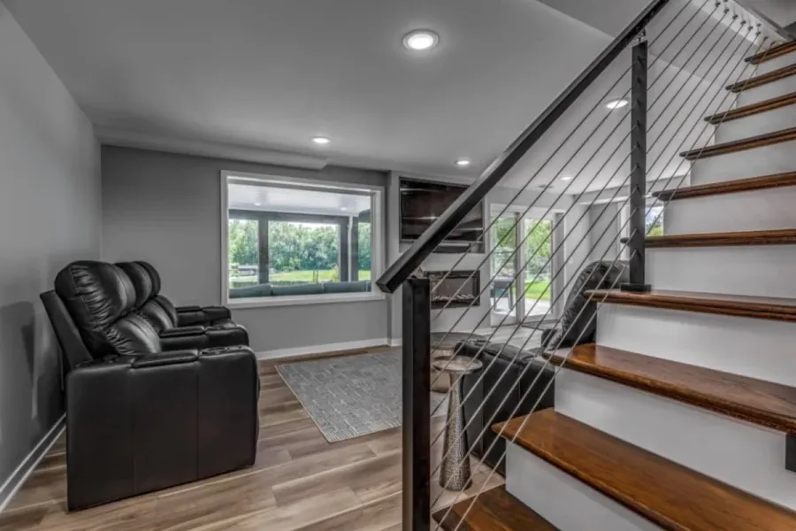Finished basement family room with black leather theater seating, wood-look flooring and a modern staircase with cable railings