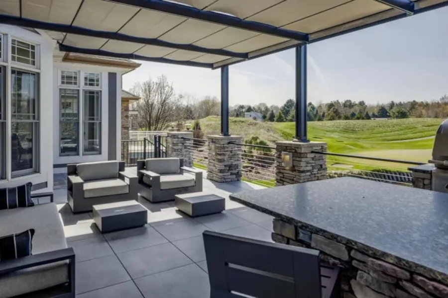 Covered outdoor living patio with a retractable pergola, stone-veneer columns, a built-in bar and lounge seating overlooking a golf course